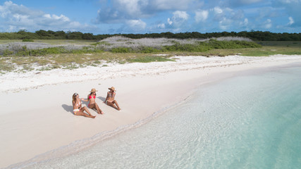 Fototapeta na wymiar three women Sitting on the white sand caribbean Beach. Drone Aerial View