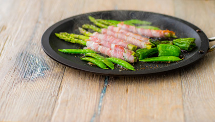 Fried asparagus wizh bacon and vegetables in a pan .