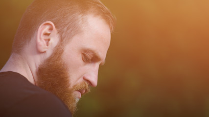 handsome young bearded pensive caucasian man looking down thinking mind outdoor portrait with copy...