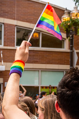 Anonymous man is waving a rainbow flag and wearing a rainbow wristband at the Gay Pride parade.