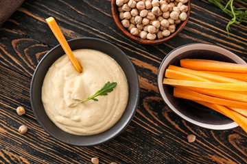 Bowl of tasty sauce and fresh carrot on wooden table