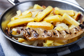 Delicious roast potatoes with onion and spices in a pan on kitchen towel on the old wooden table. Traditional rural dinner