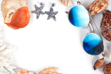 Frame border with copy space of blue sunglasses different seashells of sea molluscs and starfish earrings on white background. Flat lay, top view mockup.