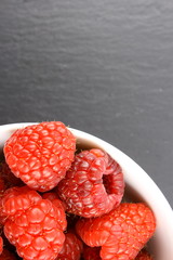 fresh red raspberry fruits in a small white bowl