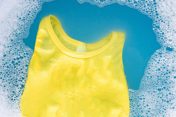 Yellow kid sleeveless shirt soak in baby laundry detergent water dissolution, washing cloth,...