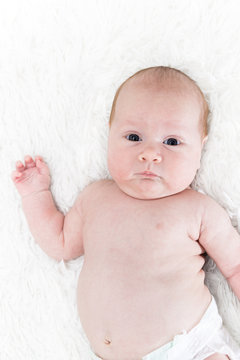 A one month old baby girl wearing a white diaper cover. Shot from overhead on a white background