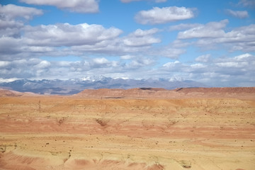 Arid climate in desert landscape against cloudy blue sky and snow capped high atlas mountain range. Ouarzazate, Morocco.