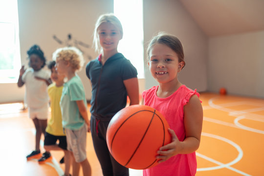 Little schoolgirl with a basketball standing near her classmates.