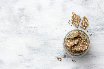 Delicious healthy multigrain gluten-free crackers, ketogenic, from chia seeds, flax, sesame and ground pumpkin seeds in a glass jar on a gray background, top view, horizontal
