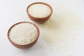 Two bowls of raw rice with scattered rice over white surface