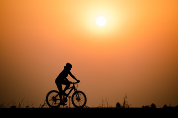 Fototapeta premium Silhouette woman cycling on sunset background