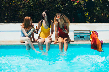 Group of friends sunbathing by the pool while drinking beer on a summer day