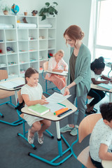 Smiling teacher handing pupils papers with tasks.