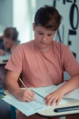 Focused pupil writing his test in a workbook.