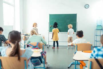 Teacher watching her class while two kids writing.