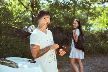 Young couple preparing for vacation in sunny summer's day. Woman and man smiling and spending time together in the forest. Concept of relationship, vacation, summer, holiday, weekend, honeymoon.