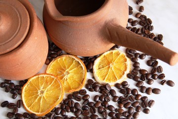 brown clay dishes, jug with handle for coffee and jug milk, a lot of roasted coffee beans and dried oranges on the grey table, close-up