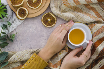 An overhead view of woman's hand holding the herbal tea cup and dried lemon on textured backdrop