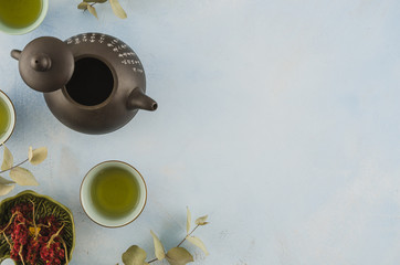An overhead view of asian traditional teapot and teacups with herbs on white background