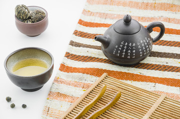 Chinese clay teapot with floral blooming tea ball tea cup against white backdrop