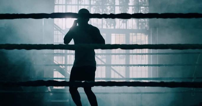Cinematic slow motion shot of a professional young muscular african man is practicing shadow boxing work out in a ring. 