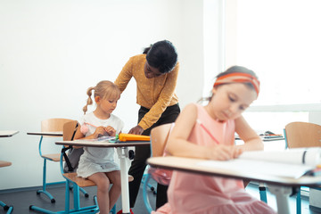 Helpful teacher wearing yellow blouse speaking with blonde girl