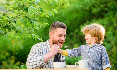 Fototapeta premium Feed son solids. Feed your baby. Natural nutrition concept. Dad and cute toddler boy having lunch outdoors. Child care. Feeding son natural foods. Feed in right way for childs stage of development