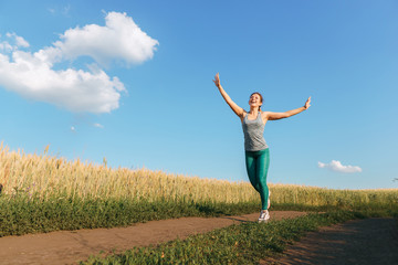 Fototapeta premium Happy woman on sunset or sunrise. Female runner raising arms expressing positivity and success.