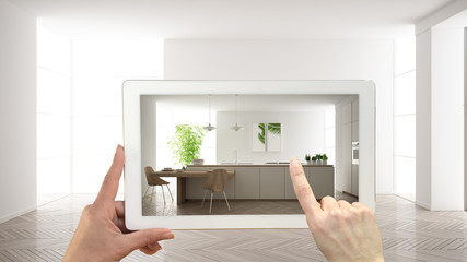 Augmented reality concept. Hand holding tablet with AR application used to simulate furniture and design products in empty interior with parquet floor, modern white kitchen