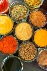  Set of spices and herbs. Indian cuisine Pepper, salt, paprika, curry, basil, mustard, nutmeg, turmeric. On a black wooden board. View from above. Close-up.