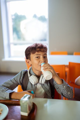 Dark-haired schoolboy with earphones on neck drinking milk