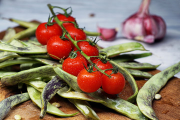 Greenbeans and cherry tomatoes in a wooden board on a rustic table.