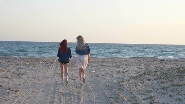 two young women go to the sea along the sandy shore back view slow motion
