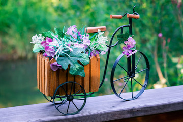 Fototapeta na wymiar Decorative small wooden bicycle with metal wheels with artificial flowers on the background of nature