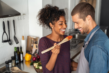 Multiethnic couple tasting food from wooden spoon