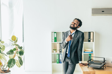 handsome afrcian american businessman standing near workplace and looking up while suffering from summer heat