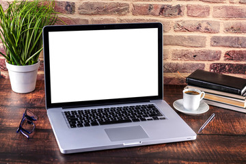 Laptop notebook with blank screen and cup of coffee and notepad pen and books on wooden table