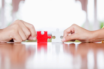 hands holding piece of red and white jigsaw puzzle. teamwork concept