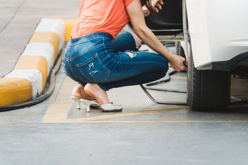 Female driver checking air pressure of car tire outdoor