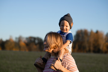 Young beautiful happy mother holds his little boy in his arms and smiles on summer sunny day....