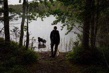 Woman with dog on lake with green tree leaves and tall grass on the shore