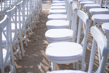Rows of white chairs in rows on the beach sand. Conference or outdoor wedding. Watching a movie or a street theater.