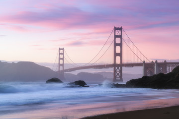 Fototapeta na wymiar Classic panoramic view of famous Golden Gate Bridge seen from scenic Baker Beach in beautiful golden evening light on sunset with blue sky and clouds in summer, San Francisco, California, USA