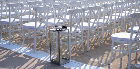 Rows of white chairs in rows on the beach sand. Conference or outdoor wedding. Watching a movie or a street theater.