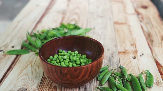 closeup of woman hand depod green peas in brown dish, on wooden table.