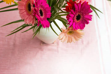 Bouquet of pink daisies in white vase on pink background, colorful flowers view above
