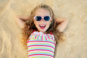 Top view of pretty little blonde girl in sunglasses lying on sandy beach during summer vacation © GVS