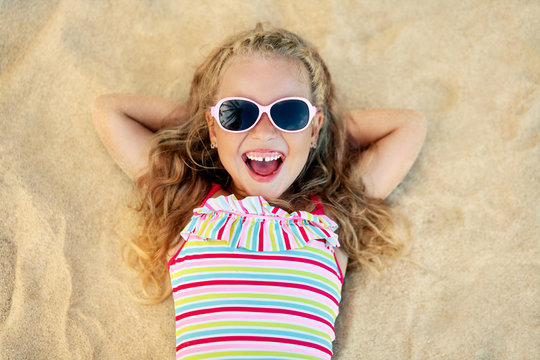Top view of pretty little blonde girl in sunglasses lying on sandy beach during summer vacation