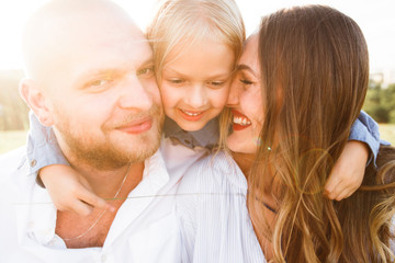 Happy family with blonde daughter smiling and hugging in nature.