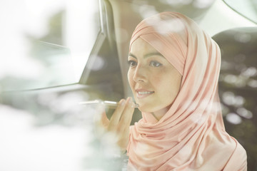 Smiling confident young Muslim businesswoman in beautiful hijab recording audio message while...